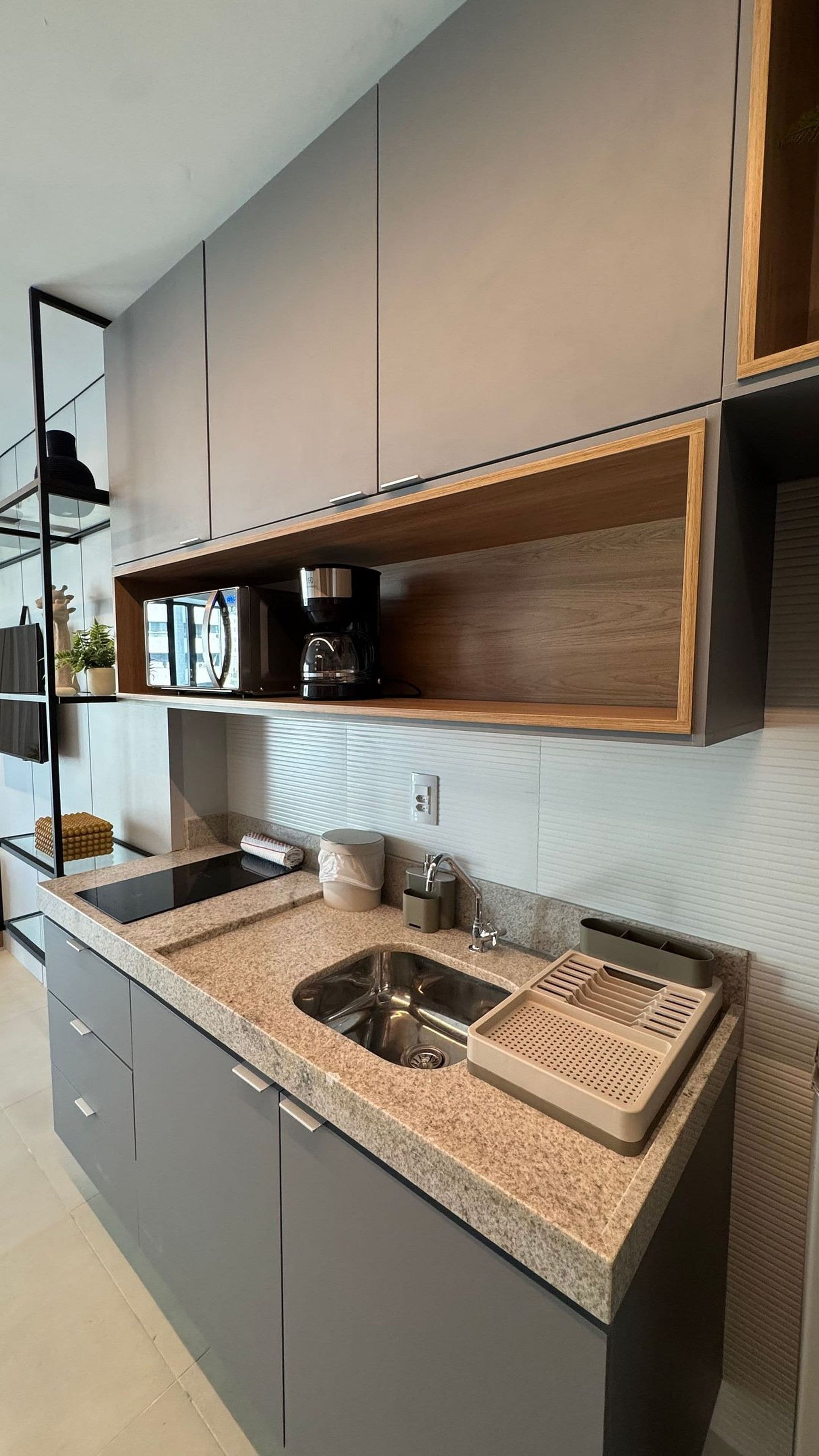 Una cocina moderna con encimera de granito, pileta de acero inoxidable y estantes de madera.