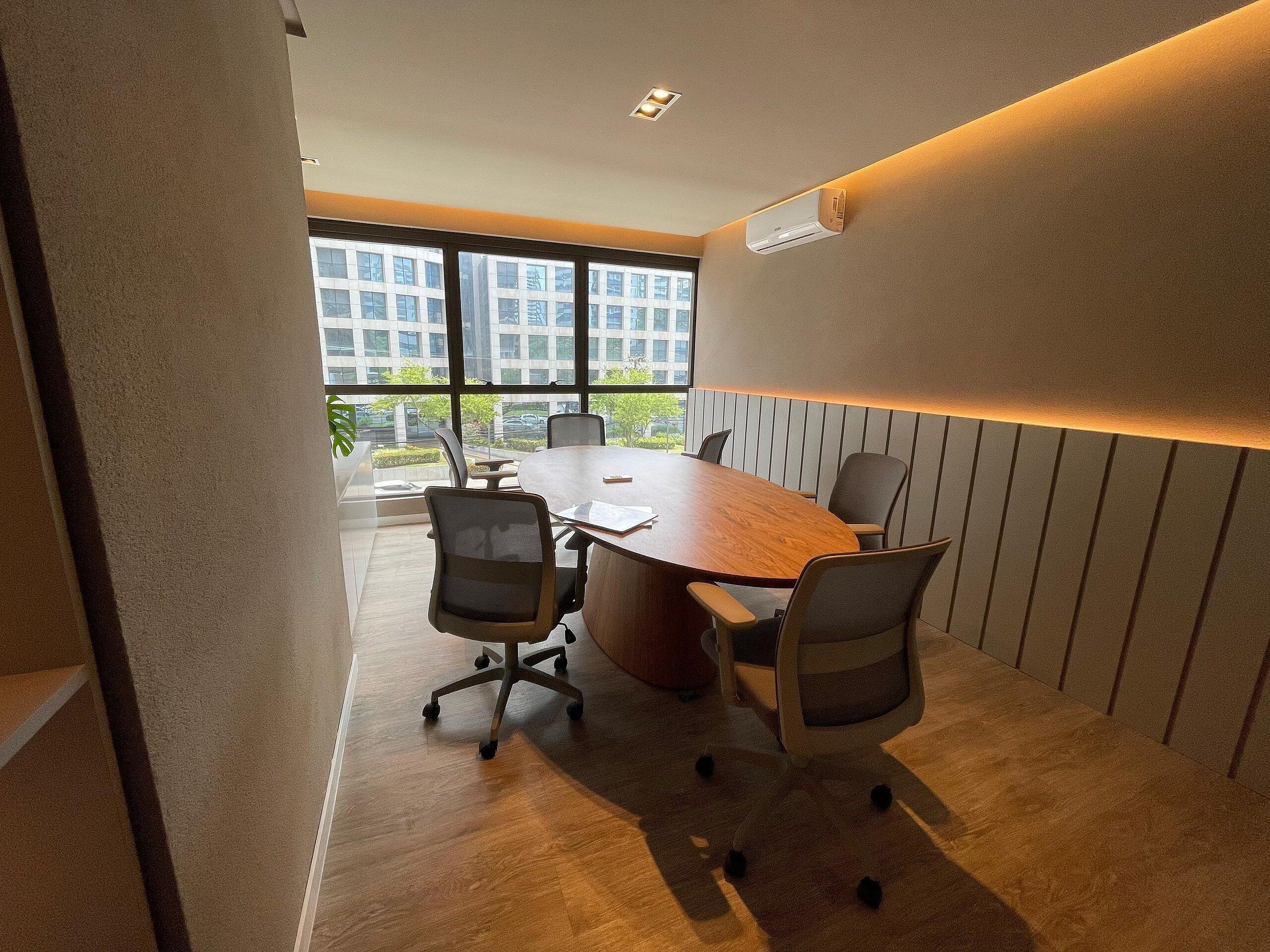A conference room with a large table, chairs, and a view of buildings through large windows.