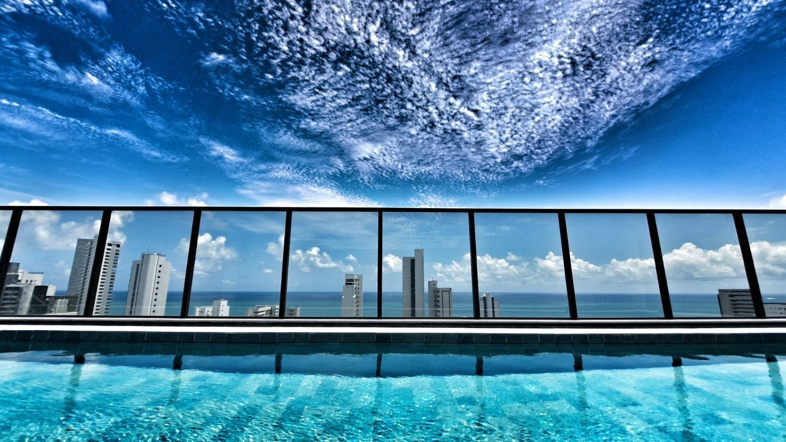 A swimming pool with a city skyline view through a glass railing.