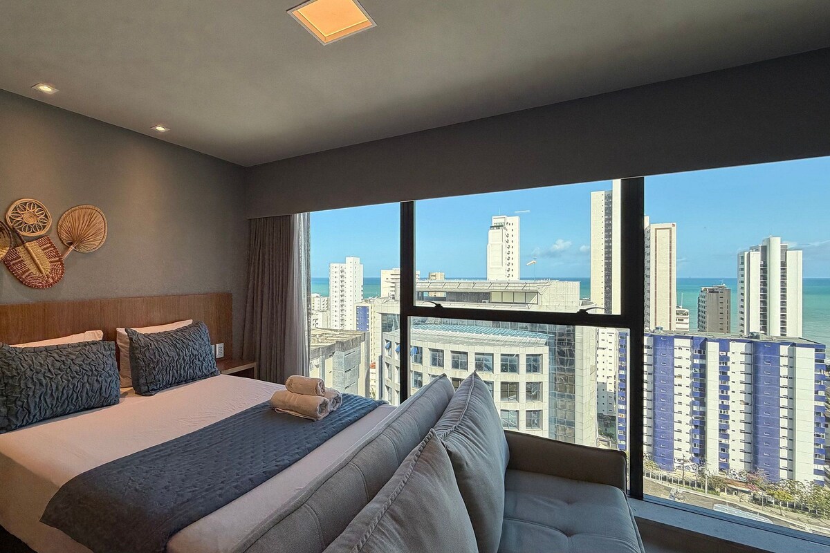 A hotel room with a large bed, a view of the city, and a cityscape through the window.