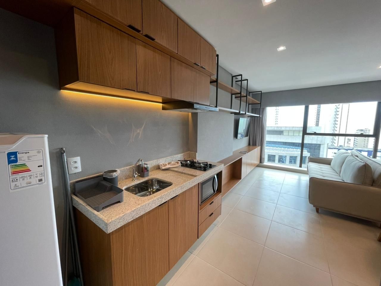 Cozinha moderna com armários de madeira, forno embutido e uma grande janela com vista para a cidade.