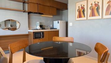 Una cocina moderna con armarios de madera, encimera negra, microondas, cafetera y refrigerador. Hay una mesa redonda con sillas y un espejo en la pared.