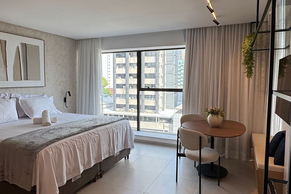 Ein modernes Hotelzimmer mit Bett, Esstisch und Blick auf die Stadtlandschaft.