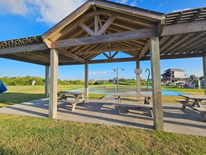 A wooden pavilion with picnic tables, a playground, and a sign indicating a splash pad operating hours.