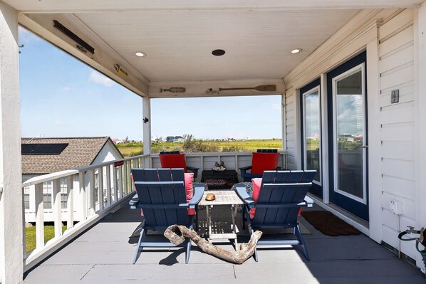 A covered outdoor seating area with two chairs and a table, a large window, and a view of the landscape.