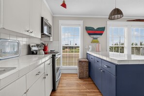 A modern kitchen with white cabinets, a blue island, and a view of the outdoors through large windows.
