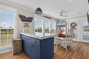 A kitchen with a central island, white cabinetry, and a view through large windows.