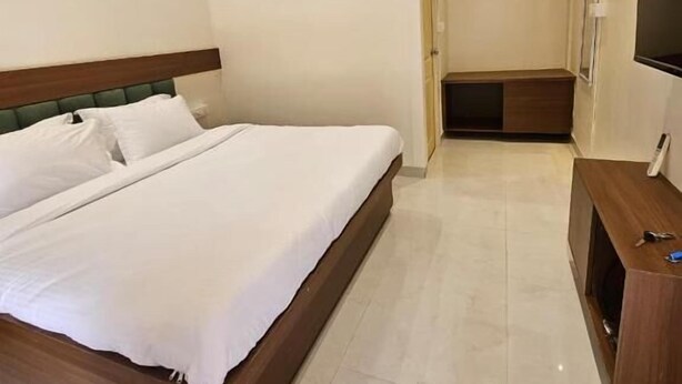 A hotel room with a bed, a wooden headboard, a TV, and a desk. - Saavi Resort Shrivardhan (Shrivardhan)