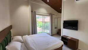 A bedroom with a bed, a television mounted on the wall, and a sliding glass door leading to a balcony. - Saavi Resort Shrivardhan (Shrivardhan)
