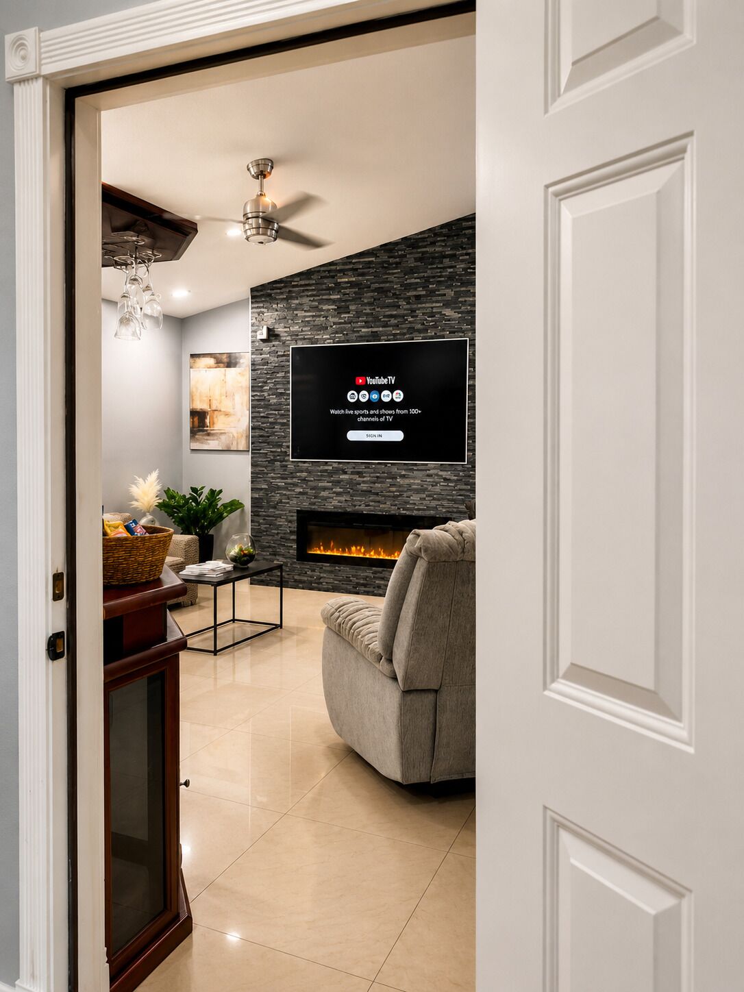 A modern living room with a fireplace, a flat-screen TV mounted on a stone wall, and a comfortable sofa.