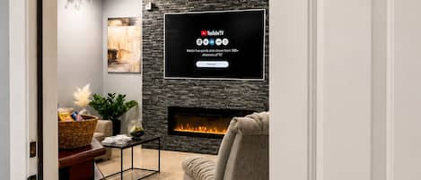 A modern living room with a fireplace, a flat-screen TV mounted on a stone wall, and a comfortable sofa.