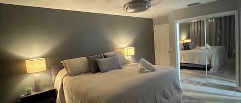 Un dormitorio moderno con una cama grande, lámparas de noche, un ventilador de techo y vistas a través de una puerta corrediza de cristal.