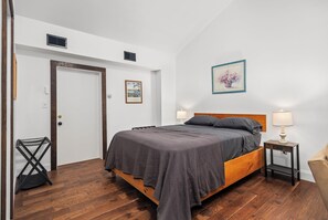A bedroom with a wooden bed, two bedside lamps, a door, and a wall-mounted picture.
