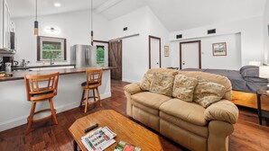 A modern kitchen with a dining area, a sofa, and a ceiling fan.