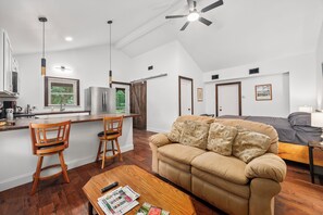 A modern kitchen with a dining area, a sofa, and a ceiling fan.