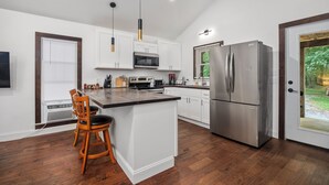 A modern kitchen with white cabinetry, a stainless steel refrigerator, and a wooden bar stool.