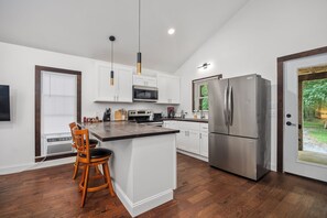 A modern kitchen with white cabinetry, a stainless steel refrigerator, and a wooden bar stool.
