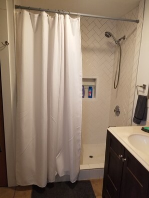 A shower area with a white shower curtain, a handheld showerhead, and a glass-enclosed shower stall. - The Shop!! (Staatsburg)