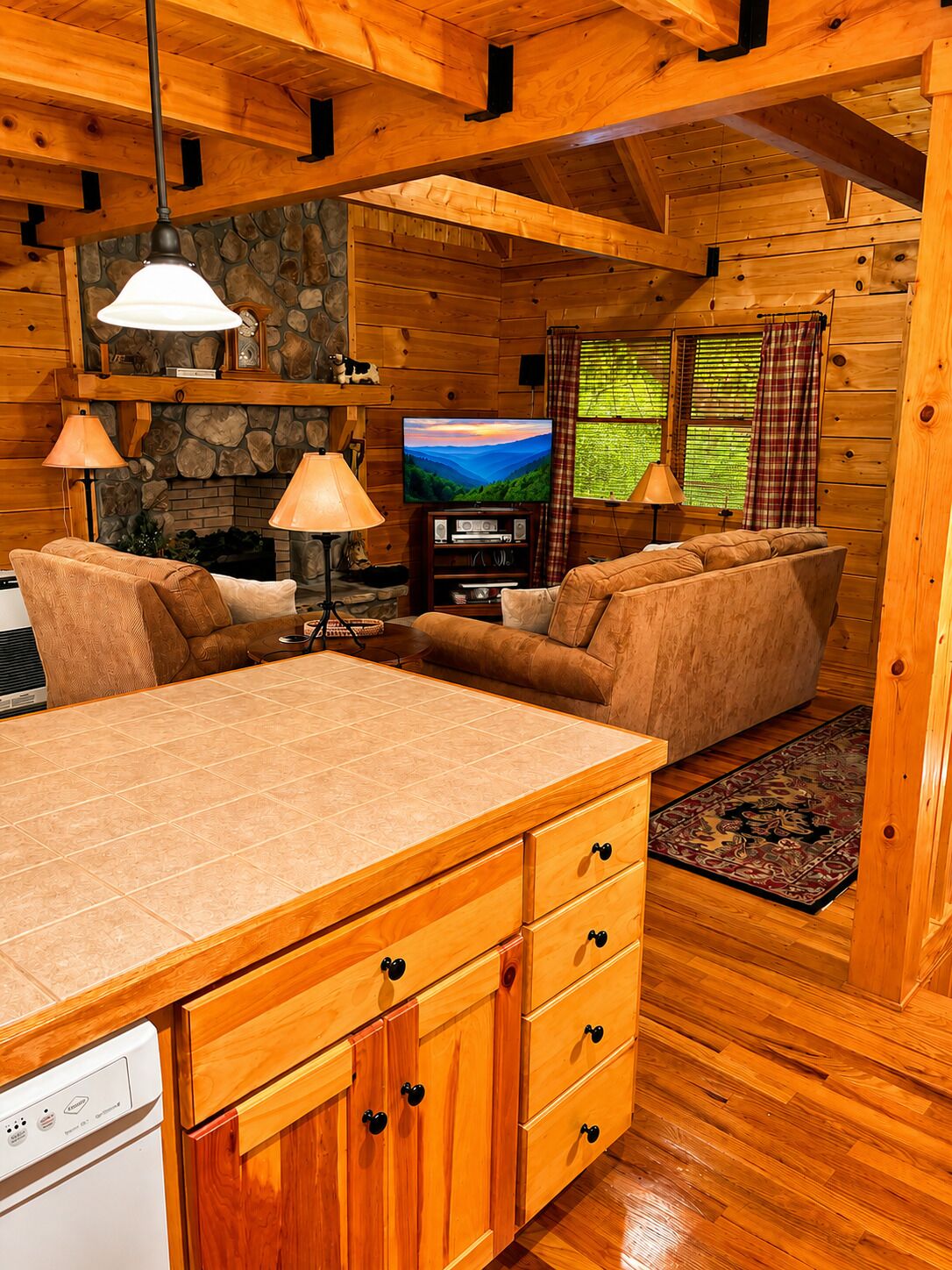 A cozy cabin interior with a stone fireplace, wooden walls, a television, and a dining area.