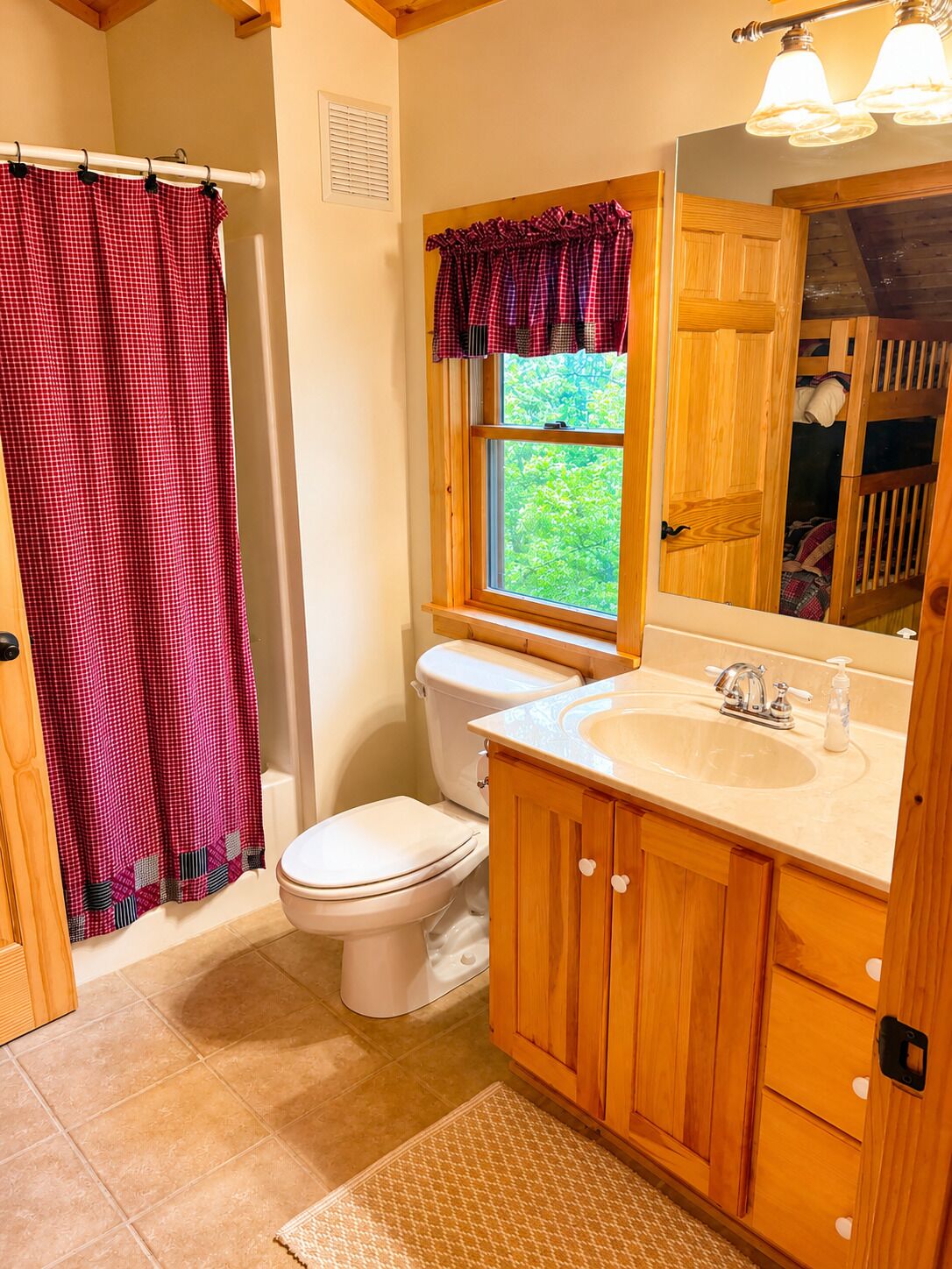A bathroom with a white toilet, wooden cabinets, a sink with a mirror, and a window with a view of greenery.