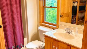 A bathroom with a white toilet, wooden cabinets, a sink with a mirror, and a window with a view of greenery.