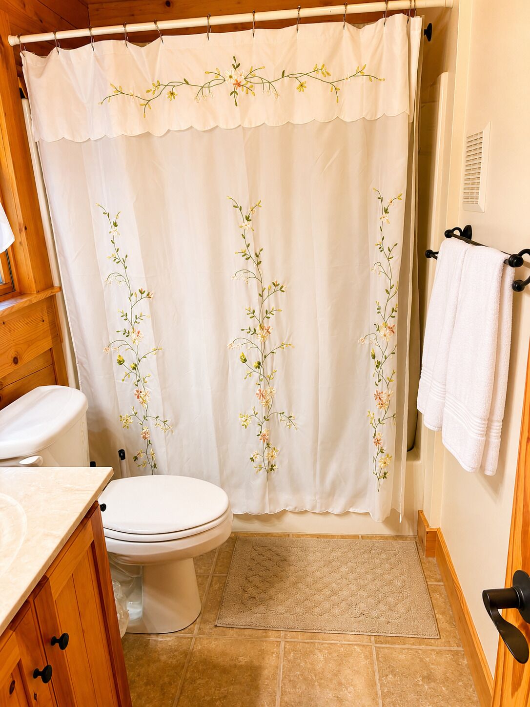 A bathroom with a toilet, a sink, and a shower curtain with floral embroidery.