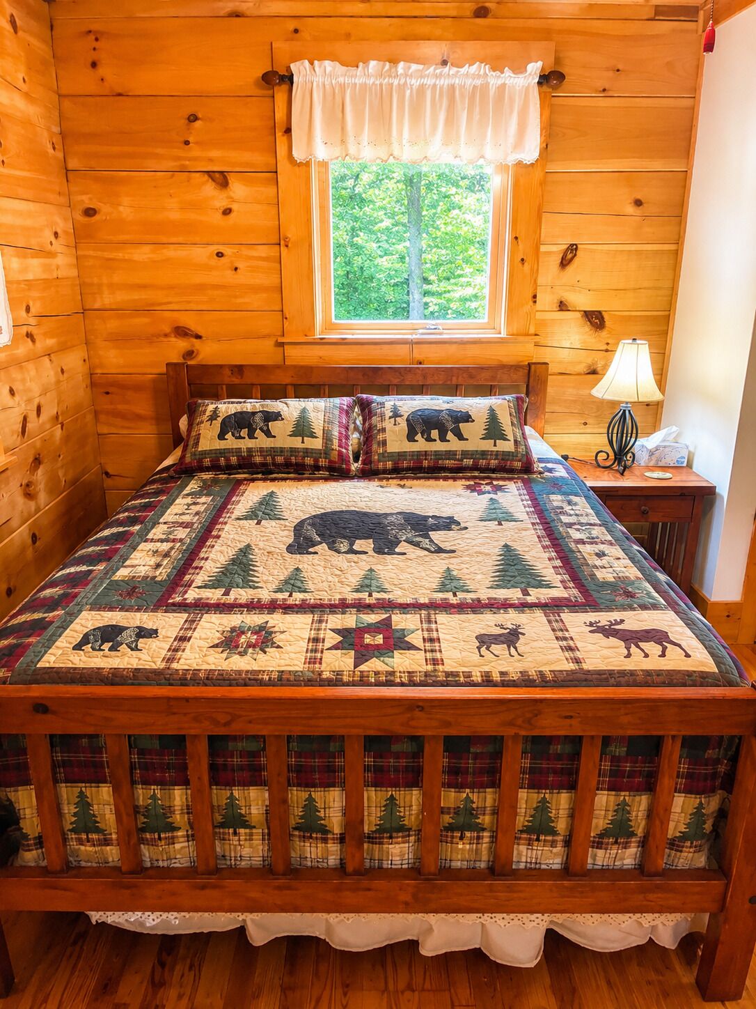 A wooden cabin bedroom with a bed, a window, and a nightstand.