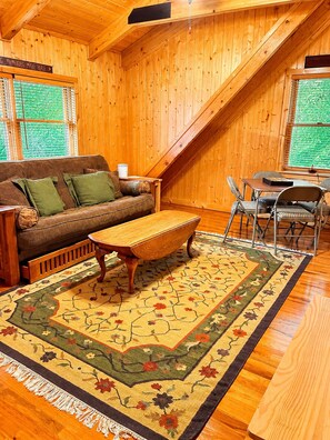 Una habitación acogedora con detalles de madera, un sofá, una mesa de centro y un área de comedor con sillas.