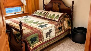 Una habitación con paneles de madera, una cama con colcha de estampados de animales, una ventana con persianas y un cesto de basura negro.