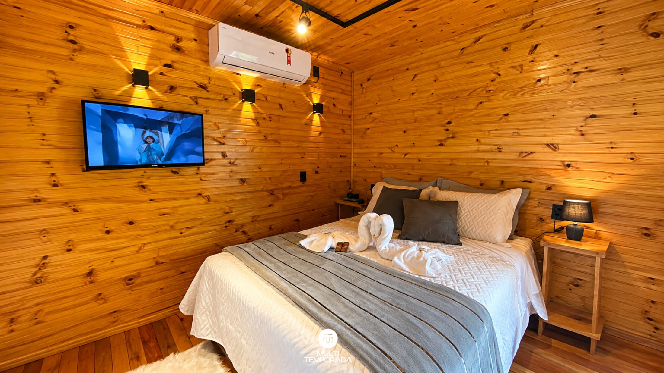 A wooden-paneled room with a bed, a television, and a nightstand with a lamp.