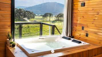 A wooden cabin with a hot tub and a view of a green landscape.