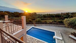 Ein Pool mit Steinrand, einer Treppe und Blick auf einen Hügellandschaft im Abendrot.