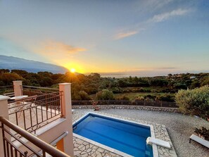 A swimming pool with a stone border, a staircase, and a view of the sunset over a hilly landscape. - Villa Dalmatia • Luxury Calm with Beautiful Sea & Mountain Views (Argostoli)