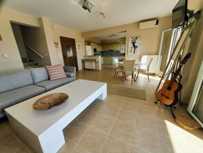 A modern living room with a sofa, coffee table, and a guitar leaning against a wall. - Villa Dalmatia • Luxury Calm with Beautiful Sea & Mountain Views (Argostoli)
