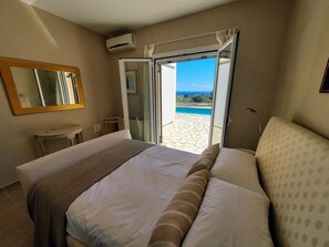 Ein Hotelzimmer mit Bett, kleinem Tisch, Spiegel und einer Schiebeglastür, die auf einen Balkon mit Blick auf den Pool führt.