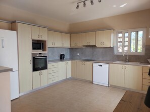 A modern kitchen with light wood cabinets, a built-in oven, microwave, and dishwasher. - Villa Dalmatia • Luxury Calm with Beautiful Sea & Mountain Views (Argostoli)