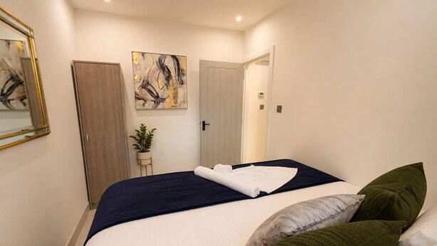 A bedroom with a bed, a nightstand, a potted plant, and a door. - Luxury 6BR Family Home 3 Bath With Hot Tub Fast WiFi (Cardiff)