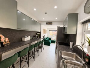 Una cocina moderna con barra, taburetes verdes, refrigerador y lavaplatos.