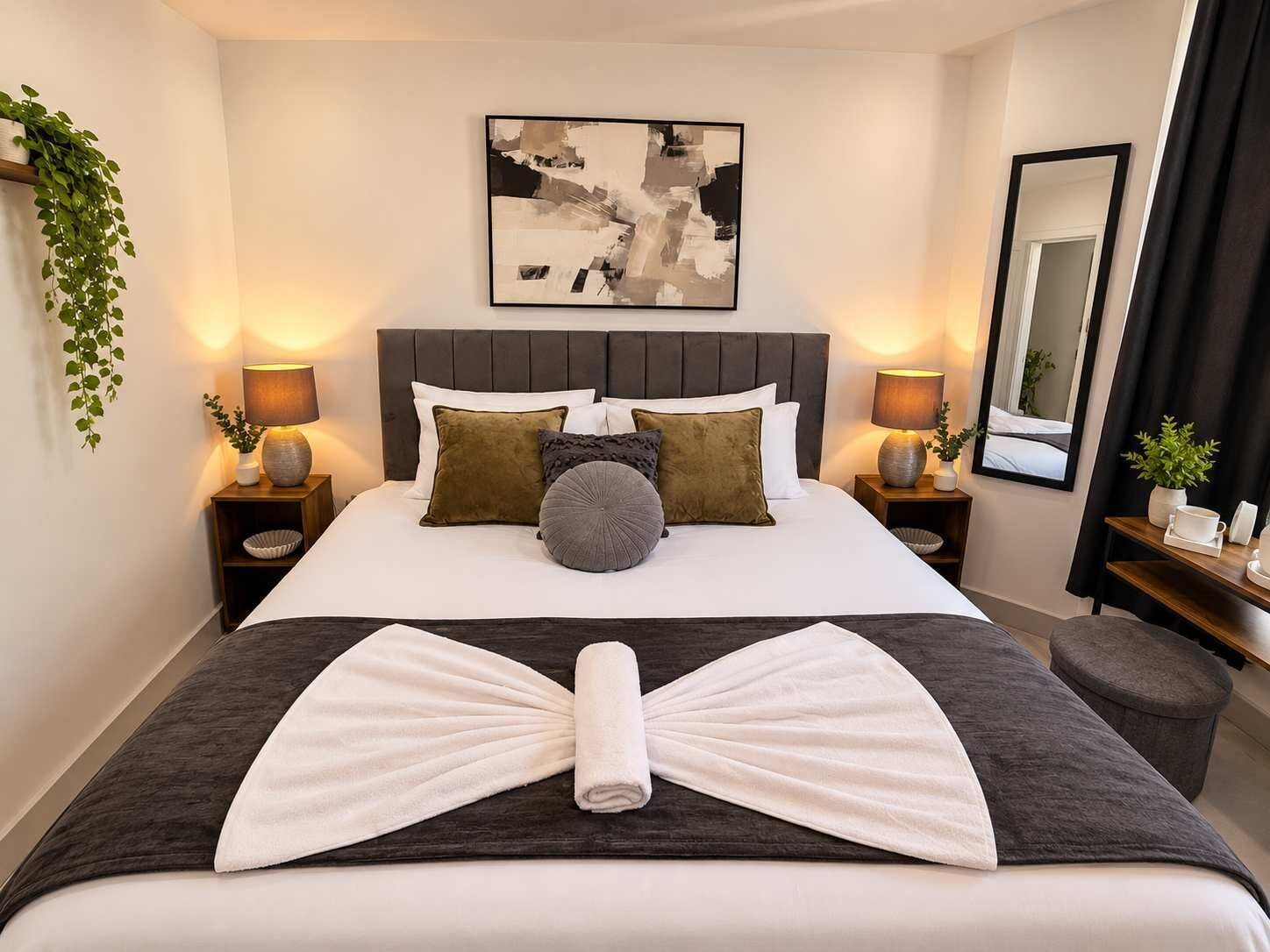 A hotel room with a neatly made bed, a large abstract painting on the wall, and a mirror reflecting the room.