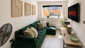 A modern living room with a green sofa, a flat-screen TV, and artwork on the wall. - Luxury 6BR Family Home 3 Bath With Hot Tub Fast WiFi (Cardiff)