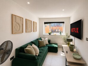 A modern living room with a green sofa, a flat-screen TV, and artwork on the wall. - Luxury 6BR Family Home 3 Bath With Hot Tub Fast WiFi (Cardiff)