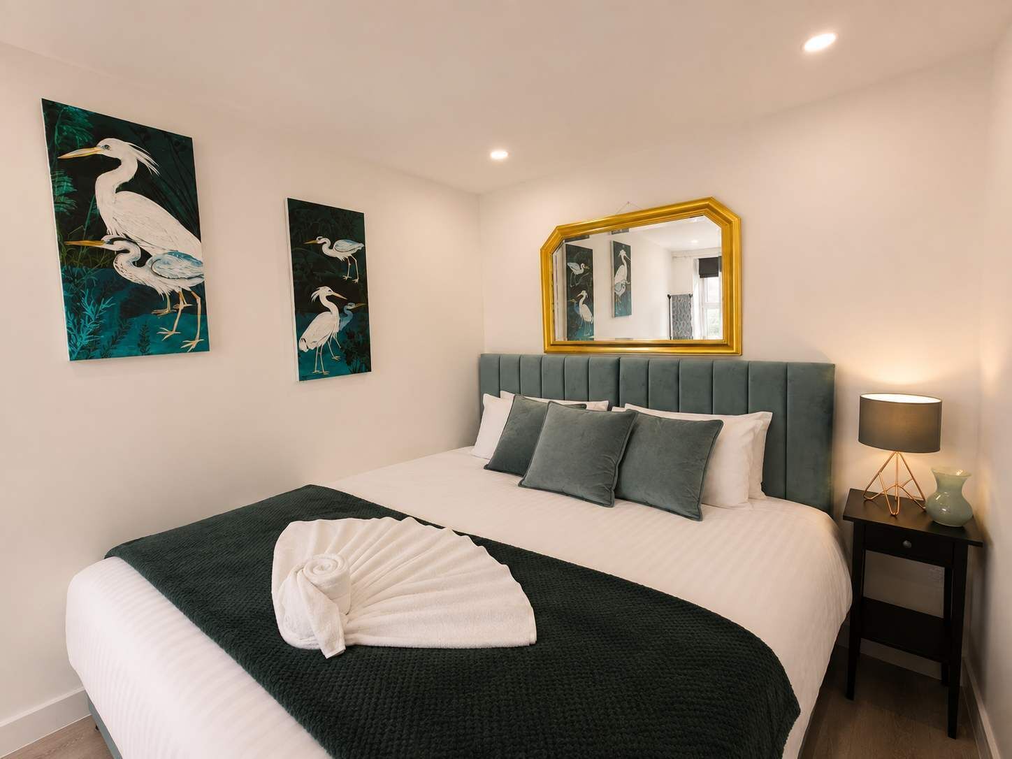 A hotel room with a bed, a bedside lamp, a mirror, and wall art.