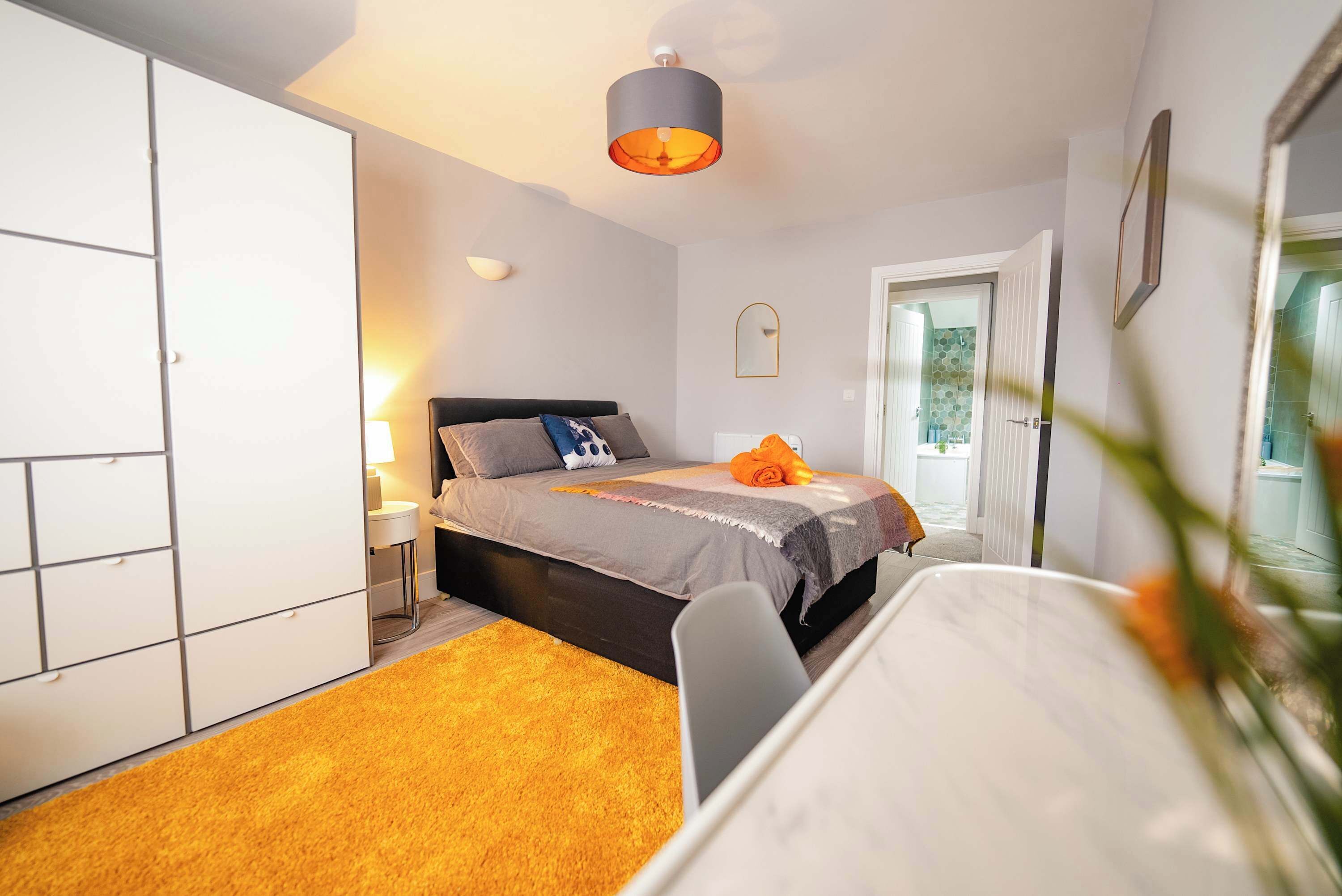A bedroom with a bed, a wardrobe, a bedside table, a lamp, and a window.