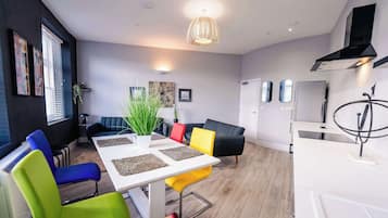 A modern living room with a dining table, colorful chairs, a sofa, and a kitchen area with a stove.