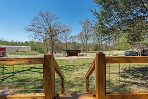 A fenced outdoor area with a wooden structure, a red building, and a car parked in the distance. - NEW 2 bed tiny home on the farm (Asheville)