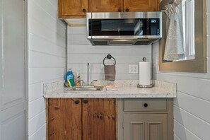 A kitchen with a stainless steel microwave, wooden cabinets, a marble countertop, a sink, and a paper towel holder. - NEW 2 bed tiny home on the farm (Asheville)