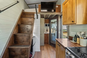 A compact kitchen with wooden cabinets, a stainless steel refrigerator, and a built-in oven. - NEW 2 bed tiny home on the farm (Asheville)
