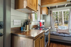 Une cuisine compacte avec des meubles en bois, une cuisinière et une fenêtre donnant sur une zone boisée.