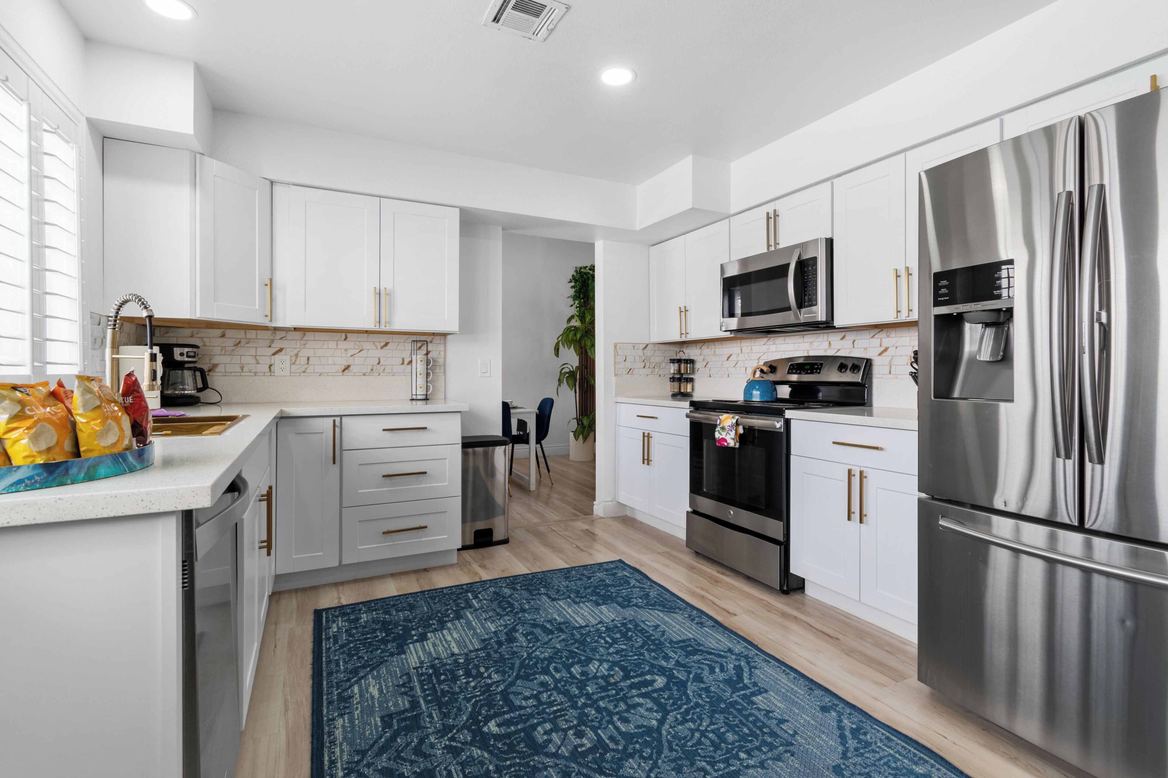 A modern kitchen with white cabinets, stainless steel appliances, and a blue patterned rug.