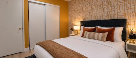 Une chambre d’hôtel avec un lit, une table de chevet, une lampe, un mur orné d’un motif géométrique et une porte.